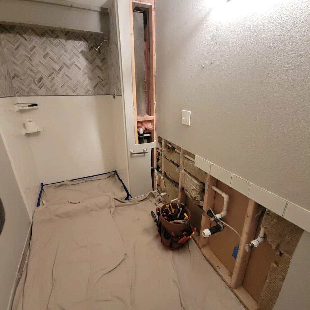 Bathroom renovation in progress with vanity removed and plumbing exposed